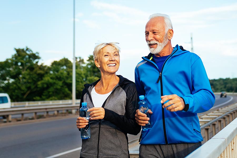Blog - Happy Senior Couple in Active Clothing Jog Along a Pedestrian Bridge