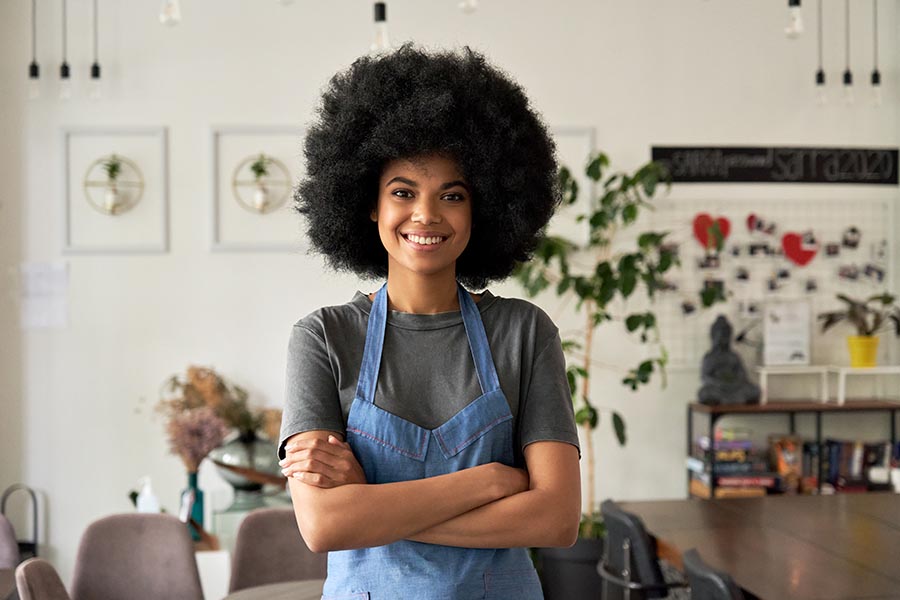 Business Insurance - Small Business Owner Standing in Her Shop, Wearing a Blue Apron, Smiling
