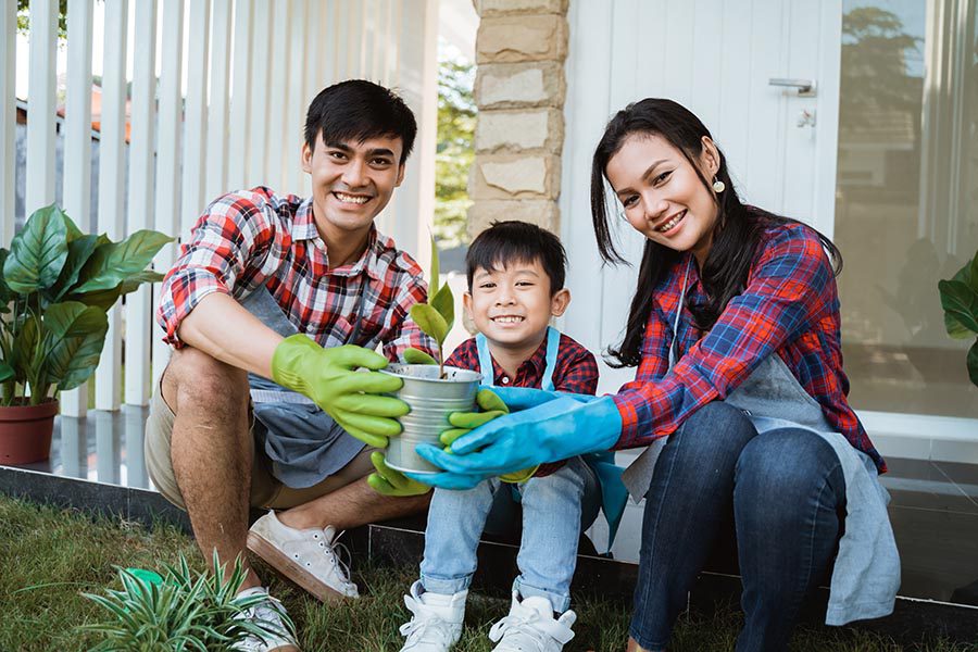 Personal Insurance - Father, Young Son, and Mother Sit on Their Back Patio, Wearing Gardening Gloves and Planting Greenery in Their Yard